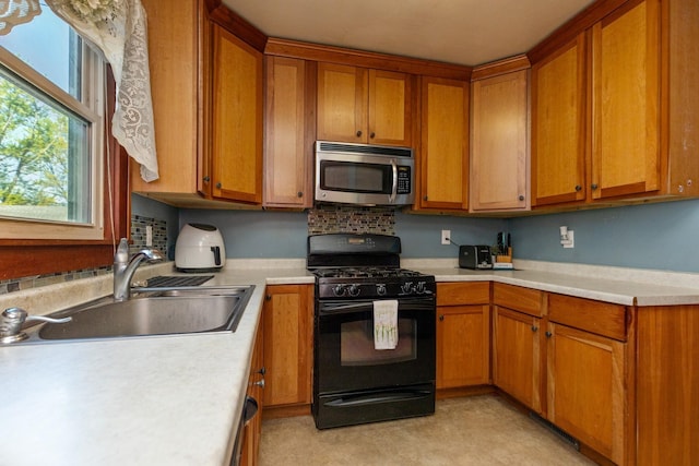 kitchen with black range with gas stovetop, stainless steel microwave, a sink, brown cabinets, and light countertops