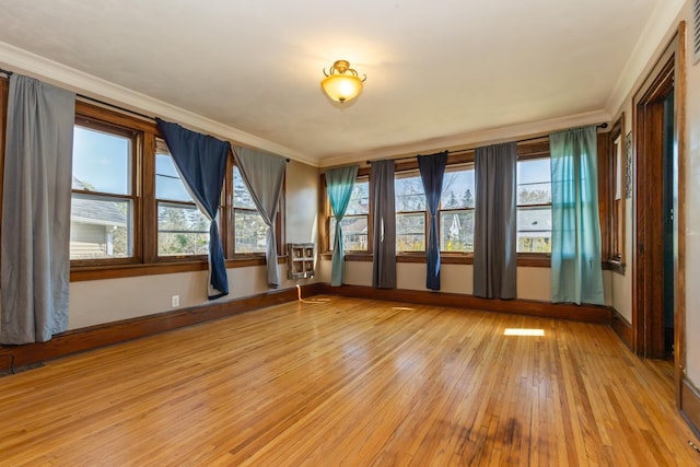 spare room featuring light wood finished floors, crown molding, and baseboards