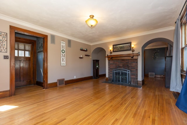 unfurnished living room featuring arched walkways, light wood-type flooring, baseboards, and crown molding