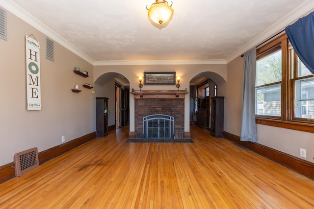 unfurnished living room with arched walkways, hardwood / wood-style flooring, baseboards, a brick fireplace, and crown molding