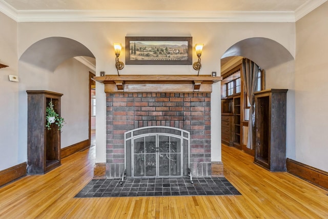 unfurnished living room featuring wood finished floors, ornamental molding, a fireplace, baseboards, and arched walkways