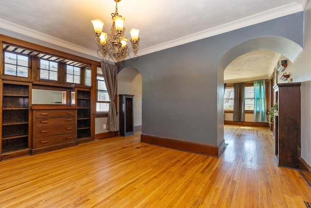empty room featuring arched walkways, light wood-style floors, baseboards, plenty of natural light, and ornamental molding