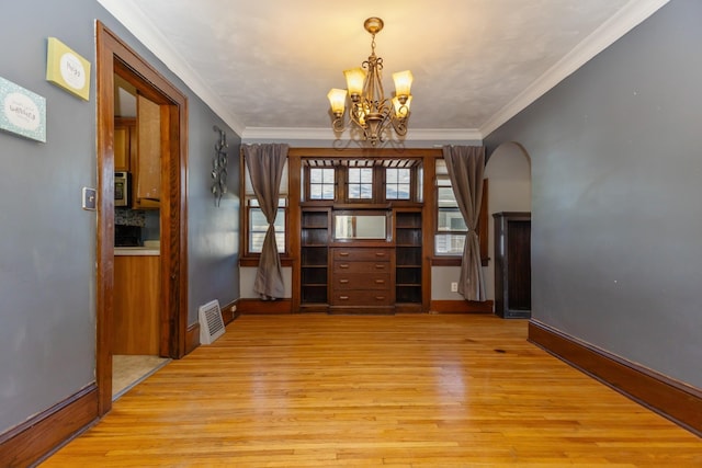 empty room featuring light wood-style flooring, a chandelier, crown molding, baseboards, and arched walkways