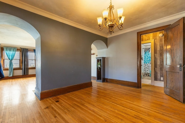 spare room with arched walkways, hardwood / wood-style floors, baseboards, a chandelier, and ornamental molding