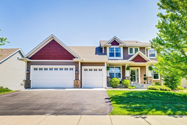 craftsman inspired home featuring asphalt driveway, a garage, stone siding, and a front lawn