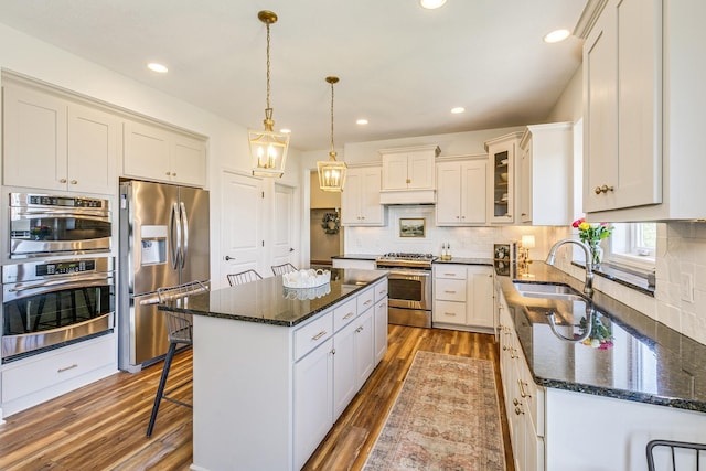 kitchen featuring appliances with stainless steel finishes, a sink, dark wood-style flooring, a kitchen island, and decorative backsplash