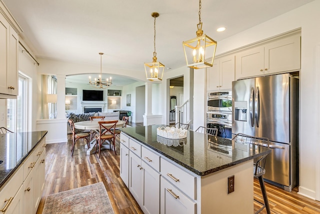 kitchen featuring stainless steel appliances, wood finished floors, decorative columns, a kitchen island, and recessed lighting