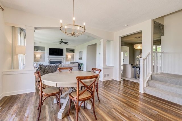 dining space featuring ornate columns, a fireplace, a ceiling fan, wood finished floors, and a chandelier