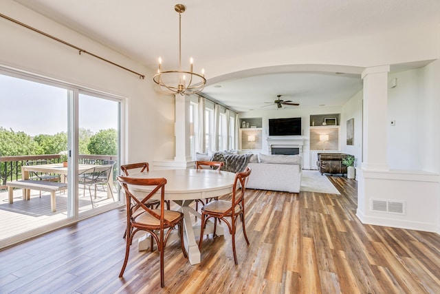 dining room featuring a ceiling fan, a fireplace, light wood-type flooring, and a chandelier
