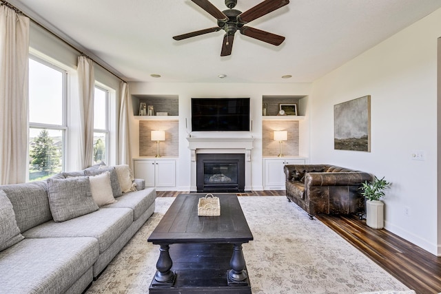 living room featuring plenty of natural light, wood finished floors, ceiling fan, and a fireplace with flush hearth