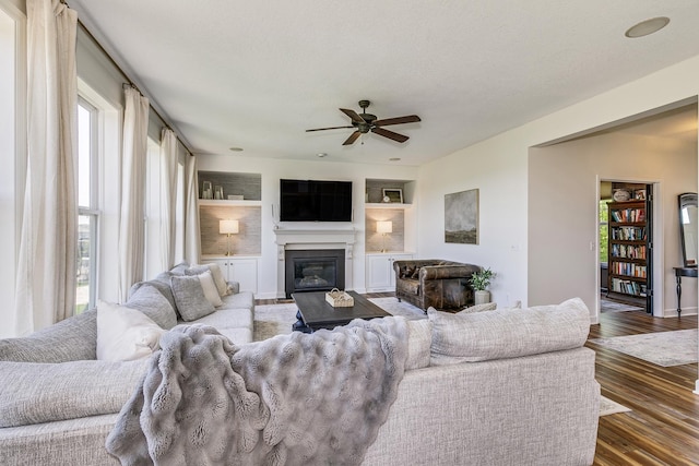 living room featuring healthy amount of natural light, a ceiling fan, a glass covered fireplace, and wood finished floors