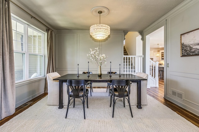 dining space featuring stairs, wood finished floors, a decorative wall, and a chandelier