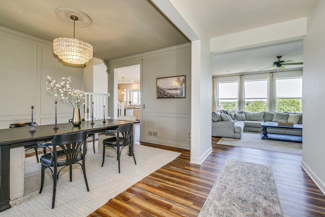 dining room featuring a decorative wall, dark wood-type flooring, a ceiling fan, a chandelier, and baseboards