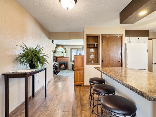 2216 County Road 15, Russell, MN 56169 - kitchen featuring a textured ceiling, freestanding refrigerator, light wood finished floors, a breakfast bar area, and a lit fireplace
