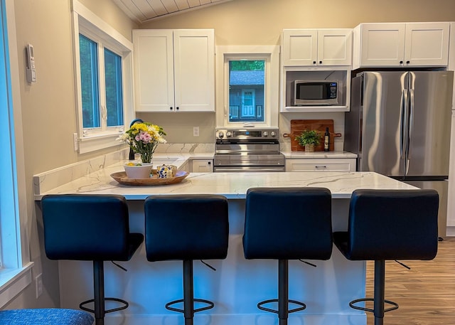 11445 State Highway 48, Trade Lake, WI 54853 - kitchen with stainless steel appliances, white cabinetry, a kitchen bar, lofted ceiling, and light stone counters