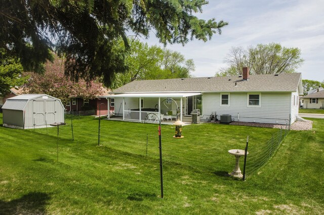 back of house featuring cooling unit, a storage unit, an outdoor structure, a chimney, and a yard