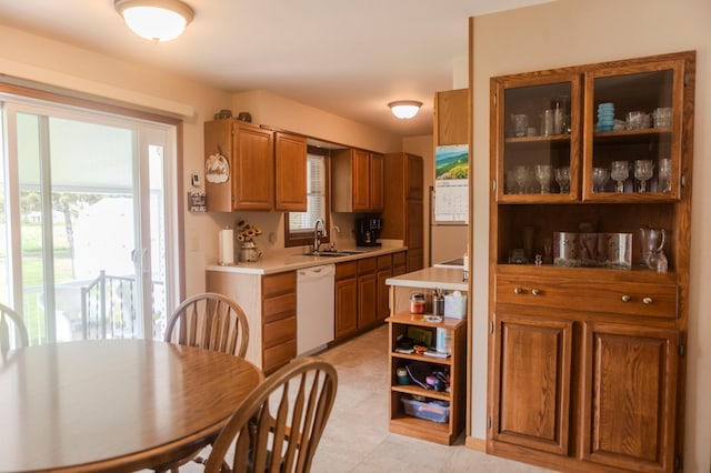 kitchen featuring dishwasher, a sink, light countertops, brown cabinets, and glass insert cabinets