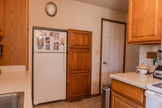 kitchen with freestanding refrigerator, light countertops, light tile patterned floors, brown cabinetry, and range