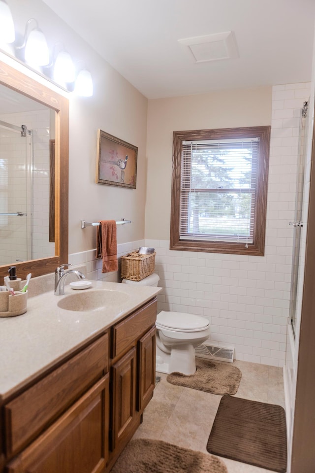 bathroom with a shower with shower door, vanity, toilet, tile walls, and tile patterned floors
