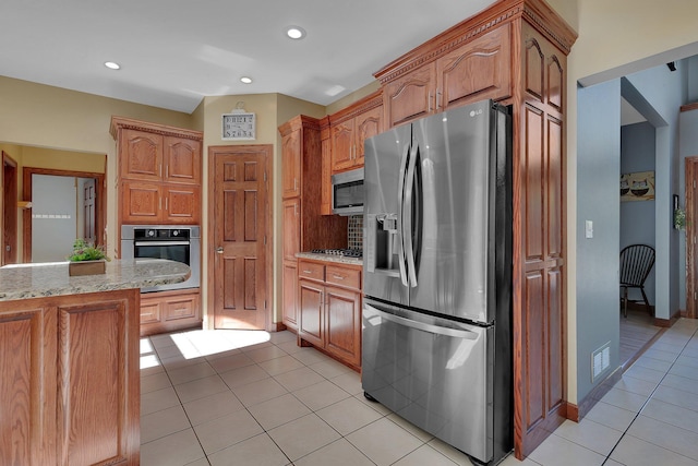 kitchen with appliances with stainless steel finishes, light stone counters, recessed lighting, light tile patterned floors, and brown cabinetry