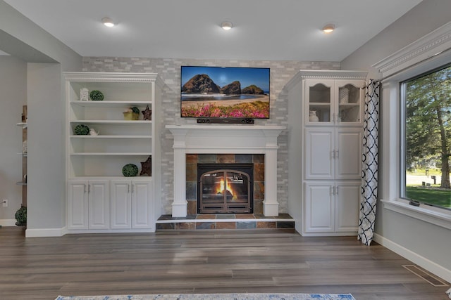 unfurnished living room featuring plenty of natural light, a tiled fireplace, baseboards, and wood finished floors