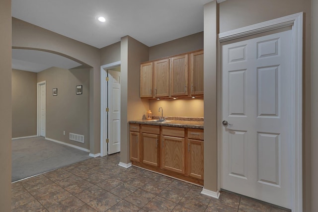 kitchen with arched walkways, a sink, baseboards, dark colored carpet, and recessed lighting