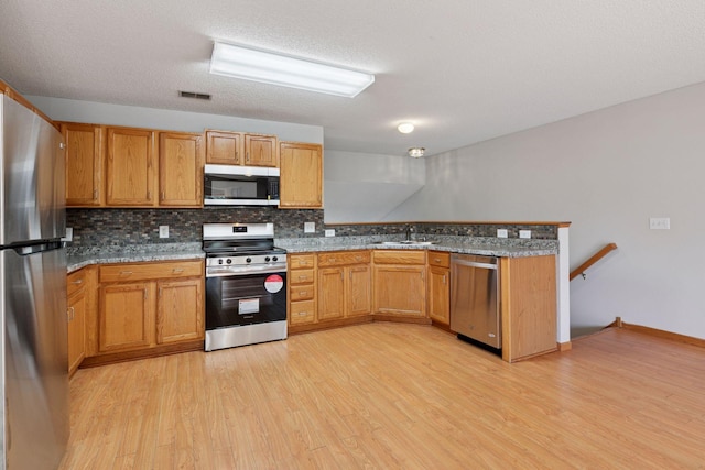 1515 Yorkshire Ln, Shakopee, MN 55379 - kitchen with stainless steel appliances, light wood-style floors, a peninsula, and backsplash