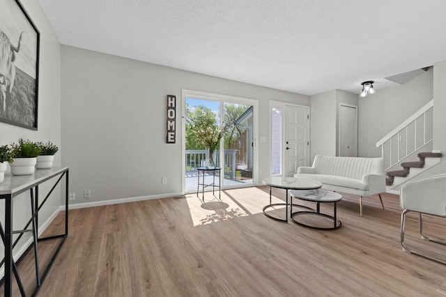 living area featuring wood finished floors, stairs, a textured ceiling, and baseboards