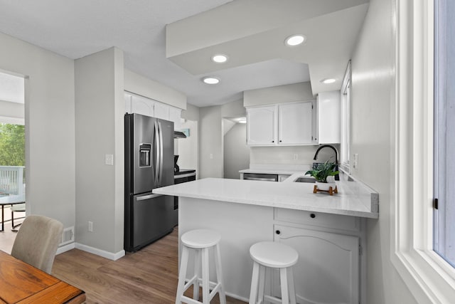 kitchen with stainless steel fridge with ice dispenser, a sink, a peninsula, wood finished floors, and white cabinetry