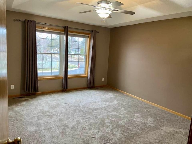 carpeted spare room featuring a ceiling fan and baseboards