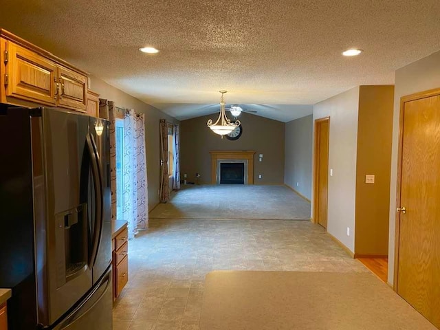kitchen with stainless steel refrigerator with ice dispenser, brown cabinets, a fireplace, a textured ceiling, and open floor plan