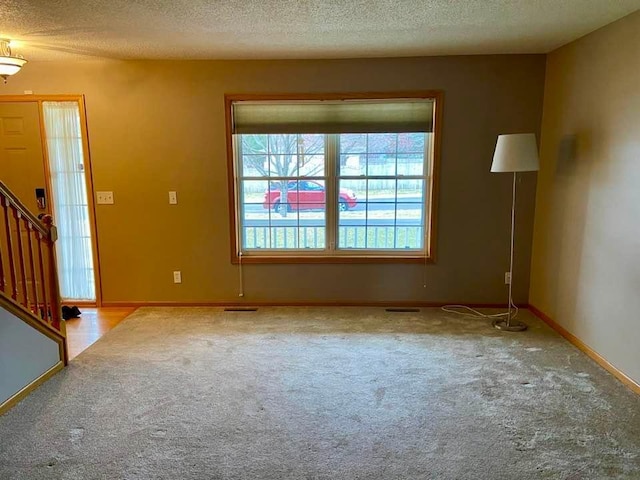 unfurnished living room featuring carpet flooring, a textured ceiling, stairway, and baseboards