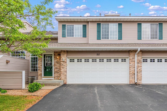 view of property with an attached garage, driveway, and cooling unit