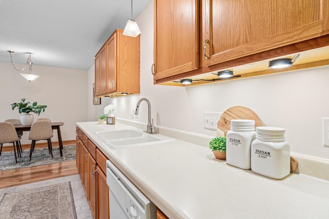 kitchen featuring a sink, white dishwasher, light countertops, and hanging light fixtures