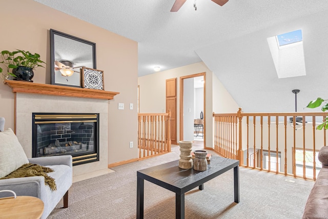living room with ceiling fan, a skylight, carpet floors, a tile fireplace, and a textured ceiling