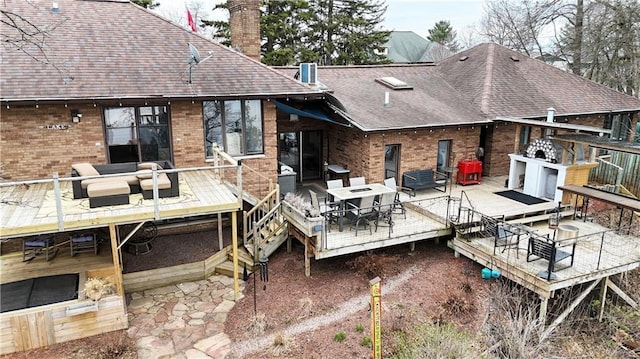 back of house with roof with shingles, outdoor dining area, brick siding, a chimney, and a deck