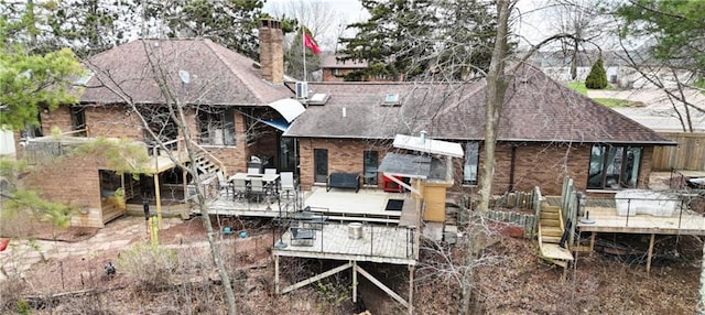 back of property with a deck, a shingled roof, brick siding, and a chimney