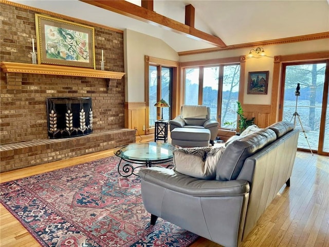 living room with vaulted ceiling, light wood finished floors, a wainscoted wall, a brick fireplace, and a decorative wall