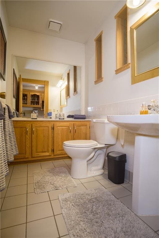 bathroom featuring tile patterned flooring, toilet, wainscoting, and tile walls