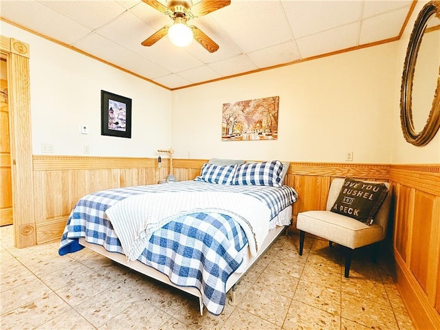 bedroom with a wainscoted wall, ornamental molding, wood walls, a paneled ceiling, and ceiling fan