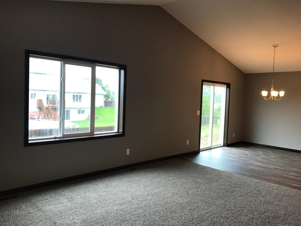 carpeted spare room featuring a chandelier, baseboards, high vaulted ceiling, and wood finished floors