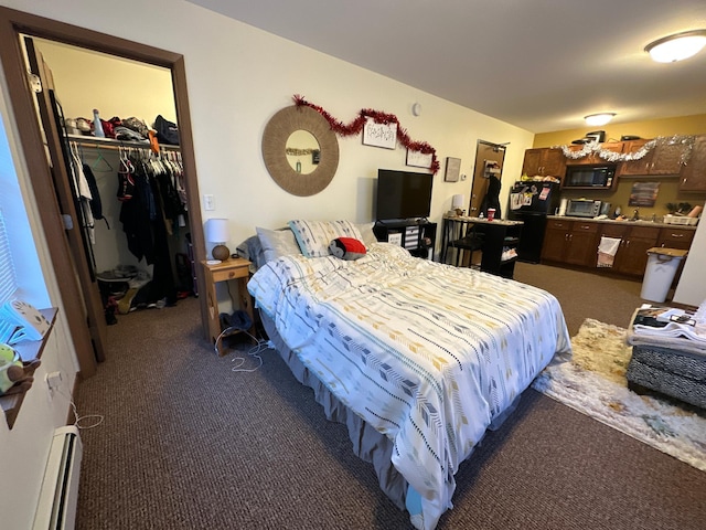 bedroom with dark colored carpet, a spacious closet, and baseboard heating