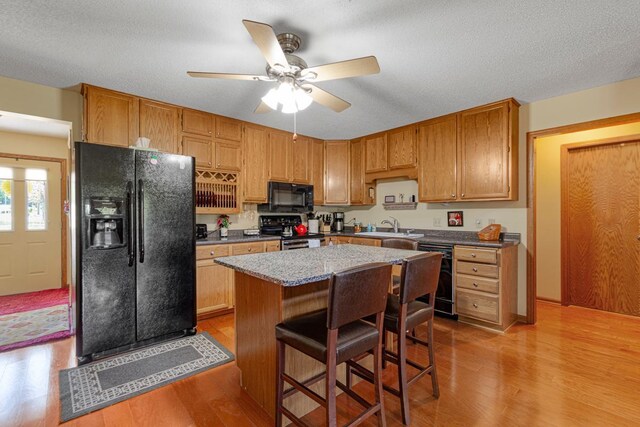 2200 15 1/2 St NW, Faribault, MN 55021 - kitchen with black appliances, light wood-style floors, ceiling fan, a breakfast bar area, and a center island