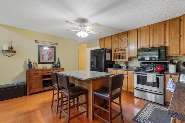 2200 15 1/2 St NW, Faribault, MN 55021 - kitchen featuring black appliances, light wood-style floors, a kitchen bar, a ceiling fan, and brown cabinets