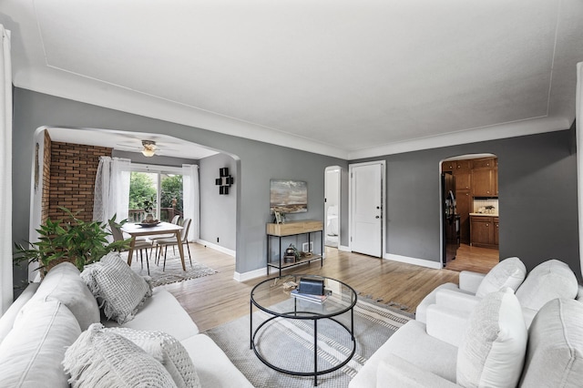 living area with arched walkways, light wood-style flooring, baseboards, and a ceiling fan