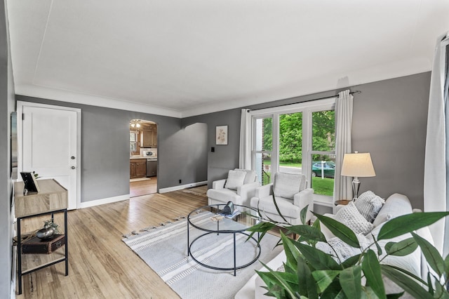 living room with arched walkways, light wood-style flooring, and baseboards