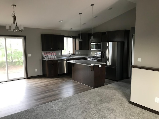 kitchen with appliances with stainless steel finishes, a kitchen island, vaulted ceiling, a kitchen breakfast bar, and a chandelier