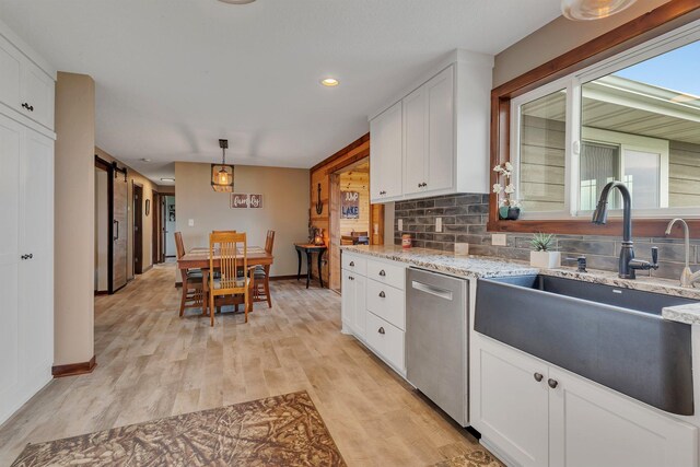 kitchen featuring dishwasher, a sink, light wood-type flooring, white cabinets, and light stone counters