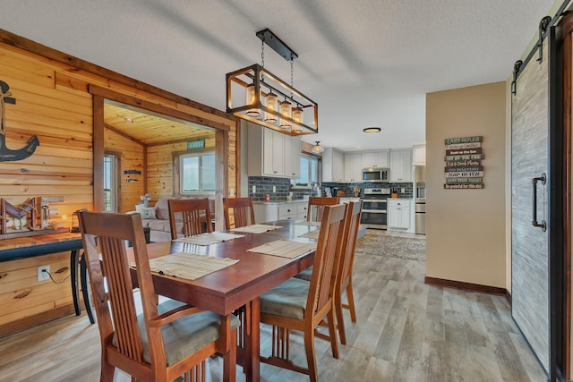 dining space featuring a barn door, light wood finished floors, wood walls, and a textured ceiling