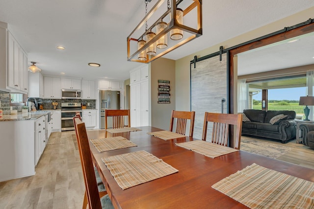 dining space with a barn door, healthy amount of natural light, light wood-style floors, and recessed lighting